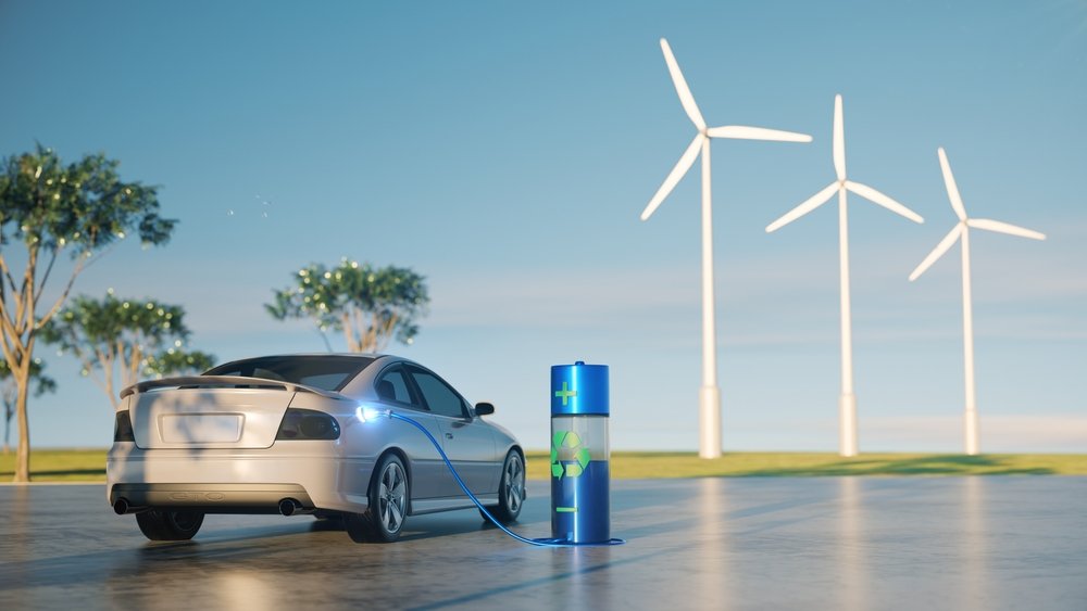 Electric car charging at a renewable energy station with wind turbines in the background.